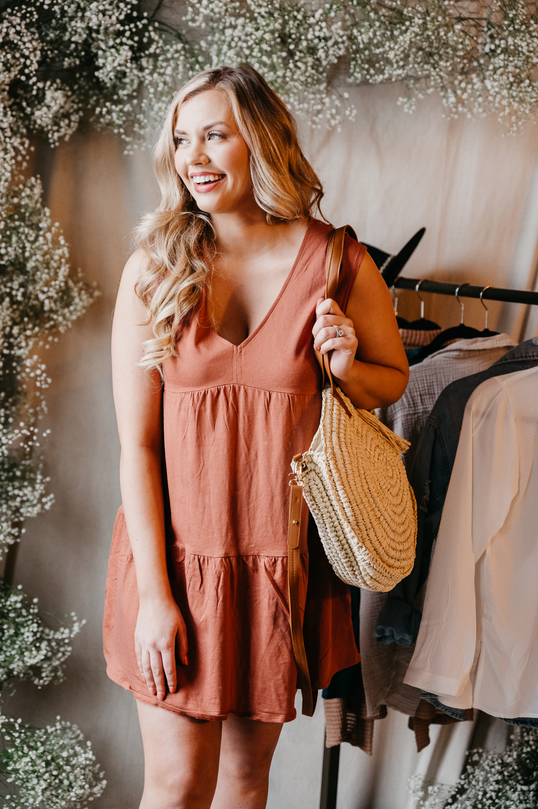 Woman in orange dress, smiling to the side and holding a bag.