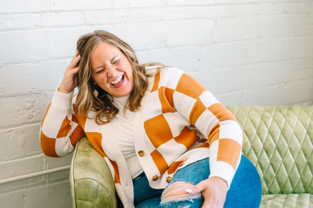 laughing woman in white and orange checkered sweater, sitting on a green leather couch