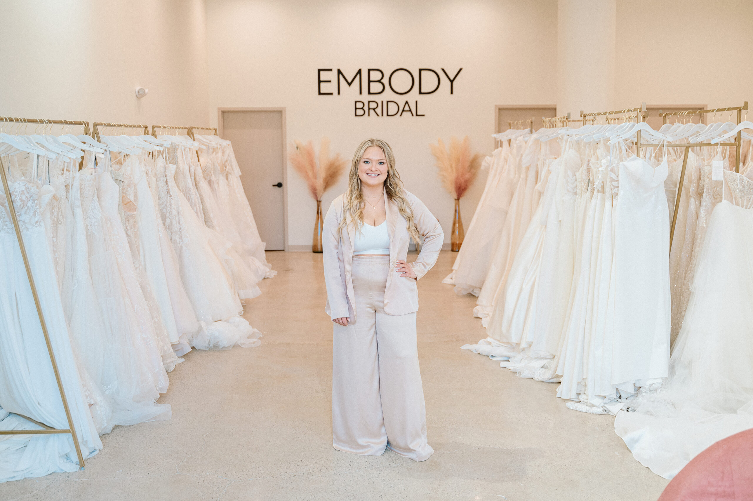 Embody Bridal owner standing between racks of wedding dresses
